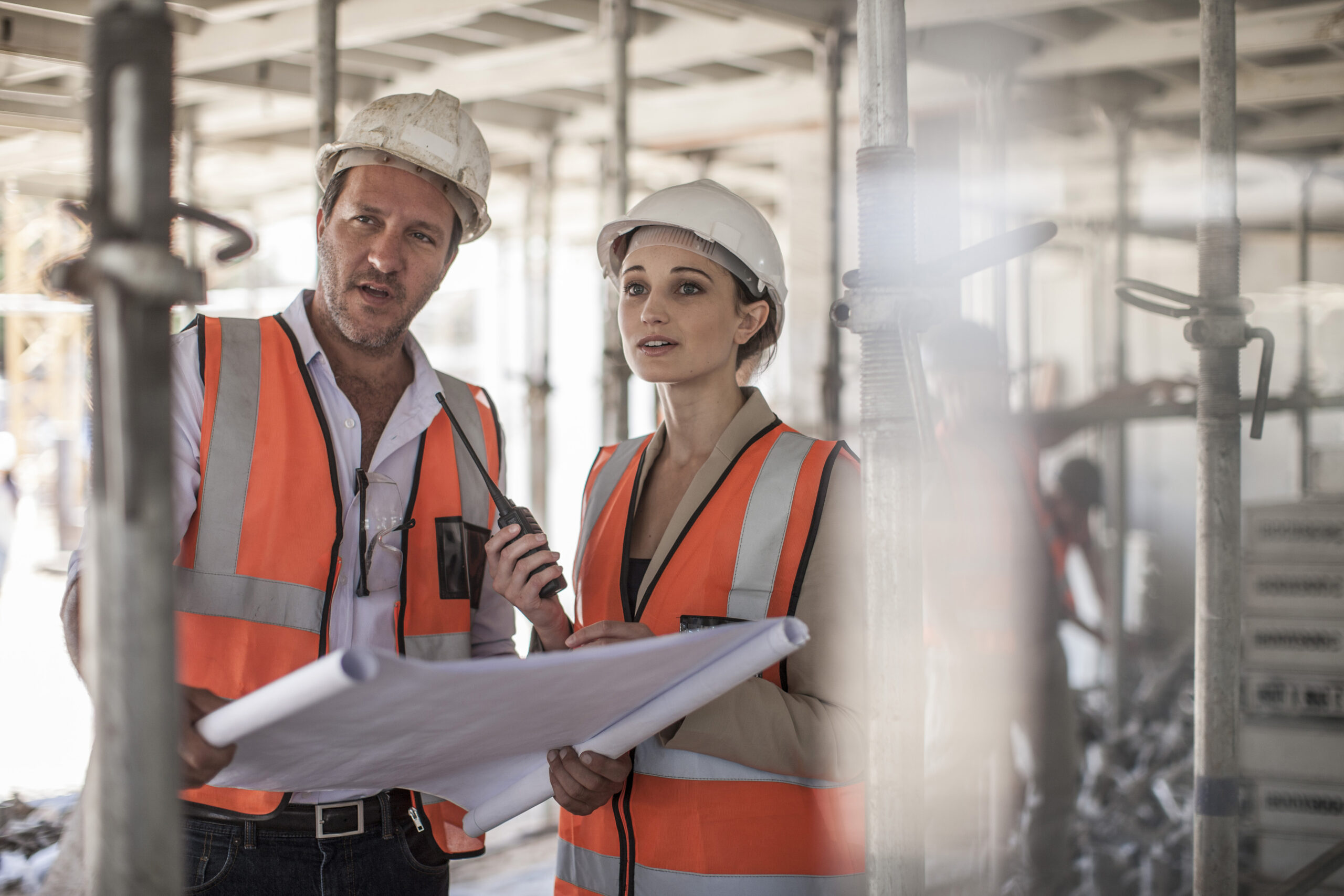 Female and male builders with blueprint on construction site